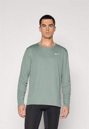 Long-sleeve, light green athletic shirt with a crew neck. Features a white Nike logo on the chest. Lightweight, smooth fabric texture.