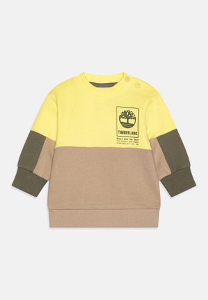 Sweatshirt coloré en blocs de jaune, marron et vert, avec un patch logo, col rond et détails de boutons sur l'épaule. Tissu doux.