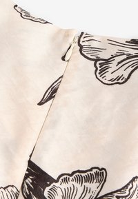 Gros plan d’un tissu beige avec imprimé floral noir et une fermeture éclair invisible cousue dans la couture.