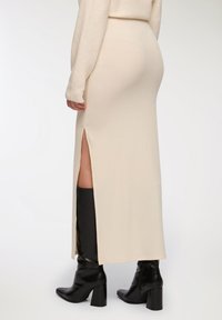 Gonna maxi a coste beige con spacco laterale, abbinata a stivali neri con tacco. Il tessuto sembra morbido e strutturato.