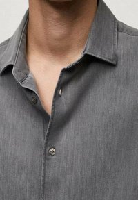 Graues Hemd mit Knöpfen aus weichem Stoff, spitzem Kragen und zwei sichtbaren Knöpfen am Hals, mit einer glatten Textur und subtiler Eleganz.