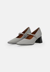 Tacones Mary Jane de cuero gris con punta afilada, correa ajustable y tacón cuadrado, con una textura suave y un interior marrón.
