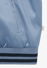 Section de veste en satin bleu clair avec une poche verticale et une ceinture côtelée avec des rayures bleu foncé et bleu clair.