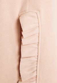 Lichtroze gebreide stof met een zijpaneel met verticale ribbeltextuur en een gerimpeld accent langs de rand. Geen aanvullende details zichtbaar.