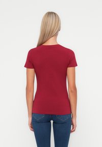 Bordo kratki rokav T-shirt s okroglo izreznico, narejen iz mehkega blaga, prilegajočega kroja, gladke teksture in brez vidnih vzorcev ali akcentov.