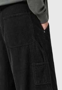 Pantaloni in corduroy neri con righe verticali e tasche laterali, caratterizzati da una vestibilità rilassata e una superficie testurizzata.