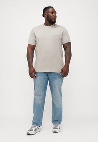 Lys grå t-skjorte med kort erme og rund hals, kombinert med blå denimjeans og grå joggesko. Enkelt design, avslappet passform.