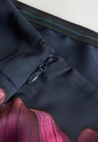 Gros plan d'une fermeture éclair noire partiellement fermée sur un tissu foncé avec un motif floral rose et violet.