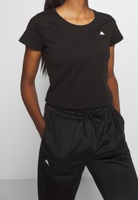 Czarna bawełniana koszulka z okrągłym dekoltem i krótkimi rękawami, zestawiona z czarnymi spodniami z elastycznym paskiem w talii, ozdobionymi subtelnym akcentem logo.
