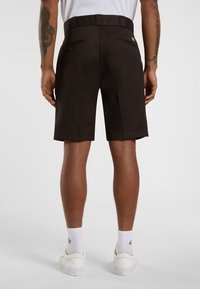 Brown shorts with a straight fit, two back pockets, and a logo tag on the waistband. Worn with white sneakers and crew socks.
