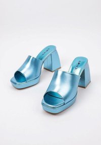 Mules plateformes métalliques bleus avec orteils ouverts, larges sangles et talons carrés épais. Texture lisse avec un minimum de détails et logo sur la semelle intérieure.