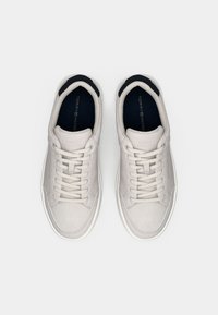 Pair of white Tommy Hilfiger sneakers with beige laces and navy blue inner soles, viewed from above on a white background.