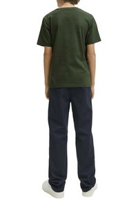 T-shirt en coton vert avec un col rond, associé à un pantalon bleu marine, affichant une coupe décontractée et un design minimaliste. Chaussures blanches visibles en dessous.