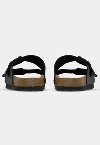 Schwarze Rutsch-Sandalen mit einem Korkfußbett, glatten Riemen, konturiertem Design und strukturiertem Außensohle mit Zickzackmuster.