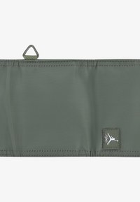 Correa de tela verde con herrajes metálicos en forma de triángulo. Presenta un borde cosido y un pequeño parche de logo con la silueta de un jumpman.