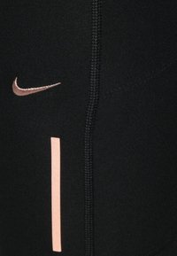 Leggings atletici neri con logo Nike rosa e una striscia verticale rosa. Realizzati in un tessuto liscio e elastico con dettagli di cucitura visibili.