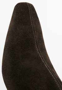 Brauner Wildleder-Hochschuh mit hohem Absatz und spitz zulaufender Spitze, mit sichtbaren Nähten entlang der Naht. Glatte Textur mit matter Oberfläche.