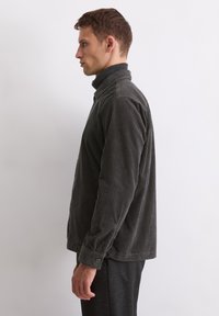 Dark grey corduroy shirt featuring a high collar, long sleeves with button cuffs, and vertical ribbed texture. Worn over black pants.