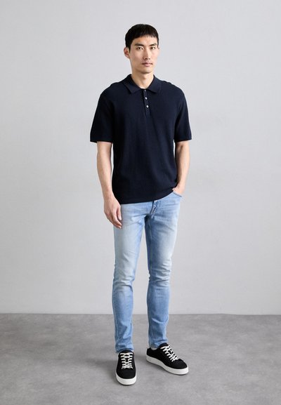 Tengerészkék, rövid ujjú polo póló, texturált mintával, világoskék, slim fit farmernadrággal és fekete, fehér talpú sportcipővel párosítva.