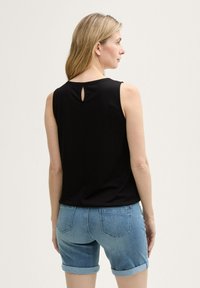 Sort ærmeløs top med en nøglehul-detalje bagpå, parret med lettet lyseblå denimshorts, hvilket fremhæver et afslappet look.