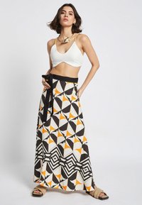 White crop top with a v-neck, paired with a long, patterned skirt featuring geometric designs in black, orange, and cream.
