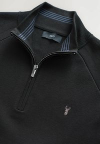 Maglione nero con zip a quarto, in tessuto testurizzato, colletto a coste, con accenti a strisce blu e un piccolo logo di cervo ricamato sul petto.