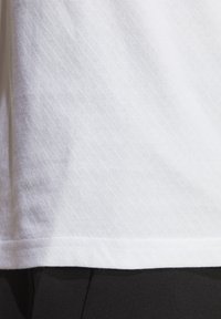 T-shirt en coton blanc avec un motif texturé subtil, un ourlet arrondi et des manches courtes ; associé à un tissu noir en bas.