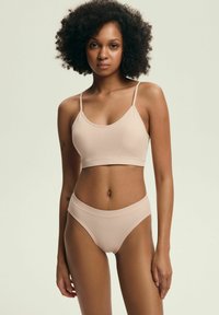 Jasnoróżowy, bezszwowy biustonosz typu bralette z cienkimi ramiączkami oraz dopasowanymi, wysokimi majtkami. Gładka, prążkowana tekstura, minimalistyczny design.