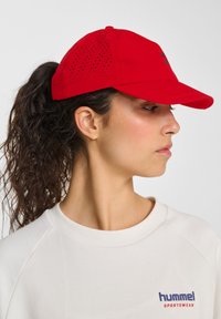 Rød baseballcap med perforeret design og buet skygge, der har et lille logo. Glat materiale og justerbar rem bagpå.