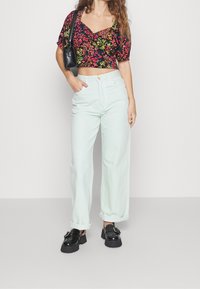 Květinový černý crop top s nabíranými rukávy, kombinovaný s širokými kalhotami v barvě světlé máty. Modelka má na sobě robustní černé platformové boty a malou černou kabelku.