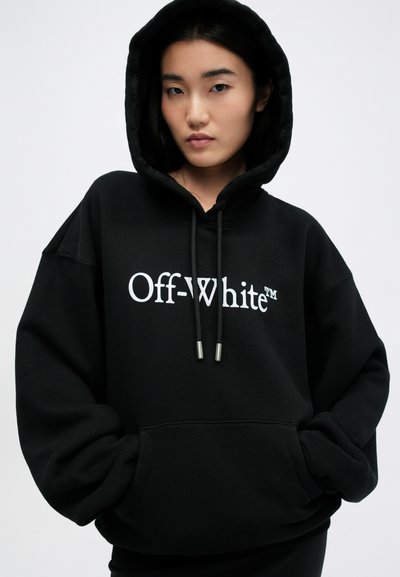 Černá mikina s kapucí od Off-White s bílým logem, volný střih, žebrované manžety a šňůrka se stříbrnými konci. Měkká textura látky.