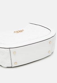 Vit axelväska med präglade blommönster, guldfärgade detaljer, rundad form och kontrasterande svarta kantdetaljer. Slät textur.