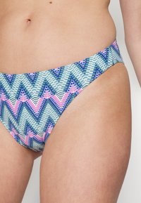 Parte inferior de bikini multicolor com um padrão geométrico de zigue-zague em azul, rosa e branco. Feita de um tecido liso e elástico com um corte de altura média.