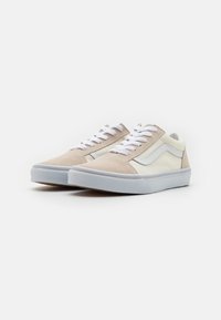 Zapatillas de gamuza beige y piel blanca con cordones blancos, que presentan una franja lateral blanca y una suela de goma gris. Superficies superiores texturizadas.