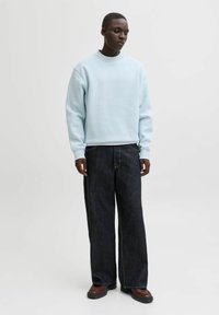 Hellblauer, übergroßer Pullover, dunkle, weit geschnittene Jeans, braune Schuhe. Weicher Stoff, Rundhalsausschnitt, legere Passform, minimalistisches Design, keine sichtbaren Muster.