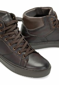 Ciemnobrązowe skórzane wysokie trampki z wyściełanym kołnierzem, okrągłym czubkiem, dopasowanymi brązowymi sznurówkami i teksturowaną gumową podeszwą na białym tle.