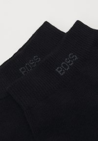 Schwarze Baumwollsocken mit gerippter Textur, versehen mit einem Logo, das am oberen Rand jeder Socke in Dunkelgrau "BOSS" liest.