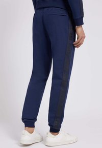 Navy sweatpants made of soft fabric, featuring an elastic waistband, tapered legs, side pockets, and a dark logo stripe down the sides.