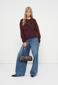 Sweatshirt bordeaux com detalhe em laço texturizado, emparelhado com jeans azul de perna larga de cintura alta e uma pequena bolsa preta.
