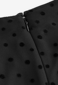 Tissu noir avec des pois en velours texturé et une fermeture éclair noire fermée à la couture.
