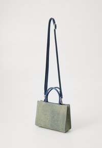 Sac à main structuré en tissu vert texturé avec une bandoulière bleue. Il dispose de deux petites poignées supérieures et d'une bandoulière amovible.