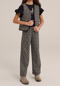Czarna i kremowa kamizelka w wzory oraz dopasowane szerokie spodnie, z czarną koszulą z białym napisem. Koszula z falbaniastymi rękawami.