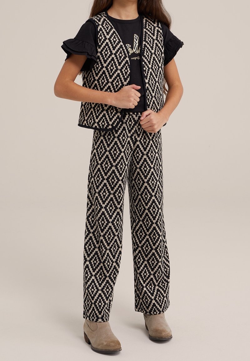 Czarna i kremowa kamizelka w wzory oraz dopasowane szerokie spodnie, z czarną koszulą z białym napisem. Koszula z falbaniastymi rękawami.