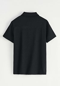Chemise noire à manches courtes avec texture côtelée et col. Présente une couleur unie et une coupe droite. Vue arrière affichée.