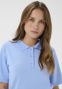 Polo bleu à manches courtes en tissu maille avec col à revers et patte de boutonnage à cinq boutons. Texture lisse et matière légère, respirante.