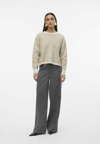 Gestreifter Strickpullover in Beige und hellbraun, cropped Design. Kombiniert mit hoch taillierten, weit geschnittenen grauen Hosen und spitzen schwarzen Absätzen.