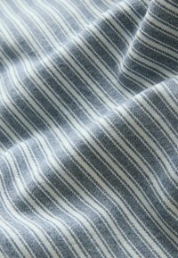 Gros plan sur un tissu doux avec des rayures verticales fines alternant bleu clair et blanc, montrant la texture et des plis délicats.