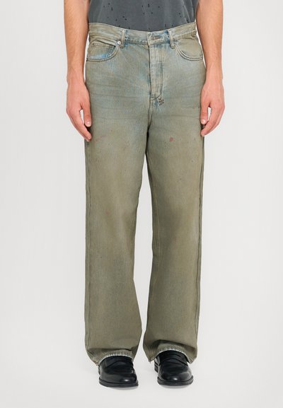 Hellgrüne, weit geschnittene Jeans aus Denim, mit einem verblassten Finish, leichten Abrieben und subtilen Flecken in der Nähe der Taschen und des Saums.
