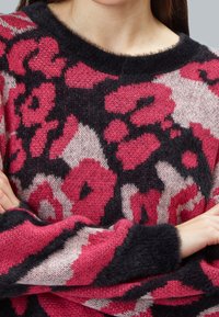 Strickpullover mit einem abstrakten Muster in Schwarz, Pink und Beige, runder Ausschnitt und weicher Textur. Manschettenärmel in dunkler Farbe.