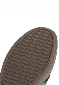 Semelle de sneaker avec un motif texturé et ondulé. Matériau en caoutchouc marron avec un contour gris clair, dotée d'un panneau latéral coloré vert.